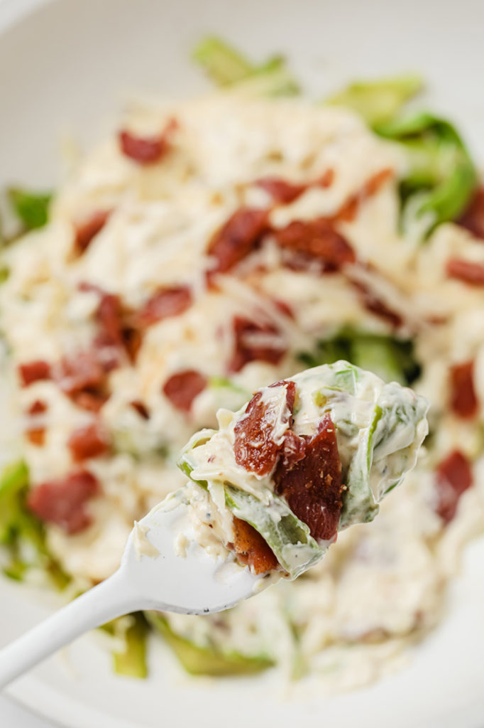 creamy asparagus pasta wrapped around white fork topped with bacon crumbles