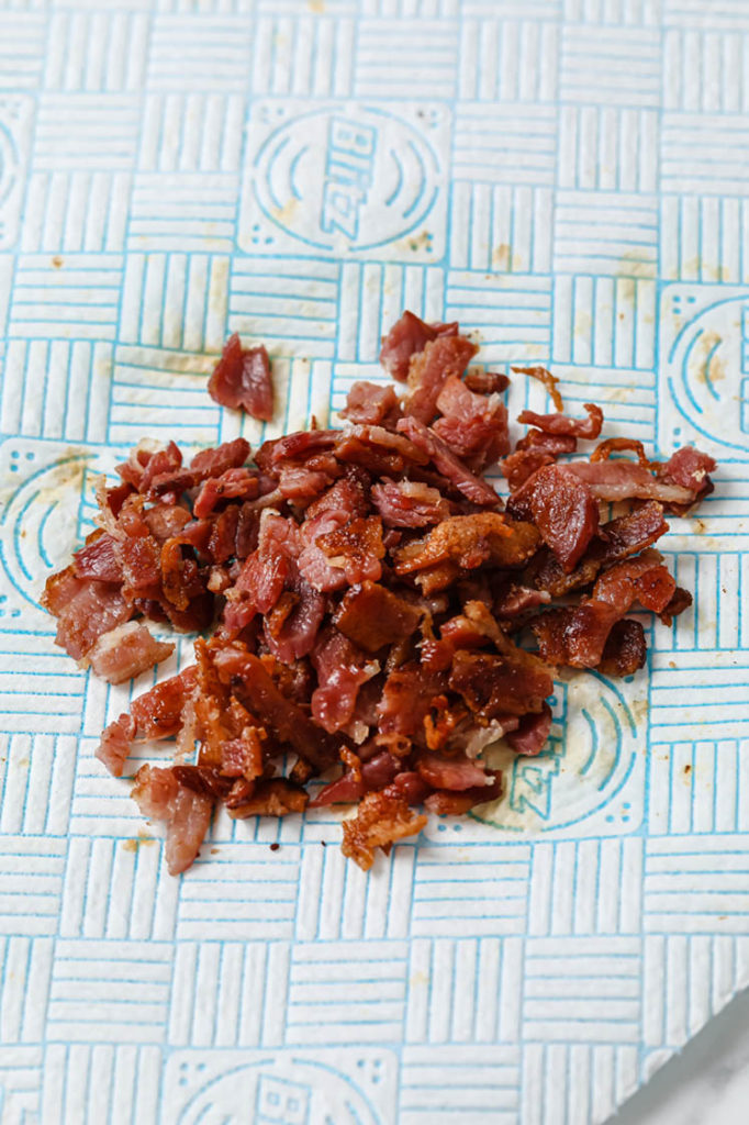 cooked bacon crumbled into pieces atop paper towel