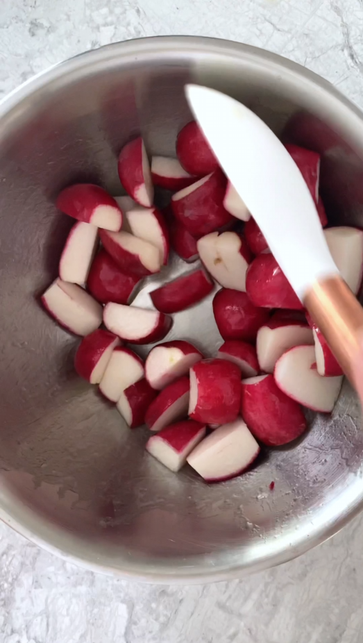 stainless steel bowl of raw radishes and avocado oil being stirred with spoon