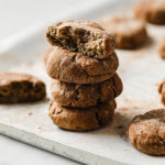 Side close-up shot of Low-Carb Snickerdoodle Cookies stacked together, resting on a baking pan. The top cookie appears to be bitten and shows the inside of the cookie.