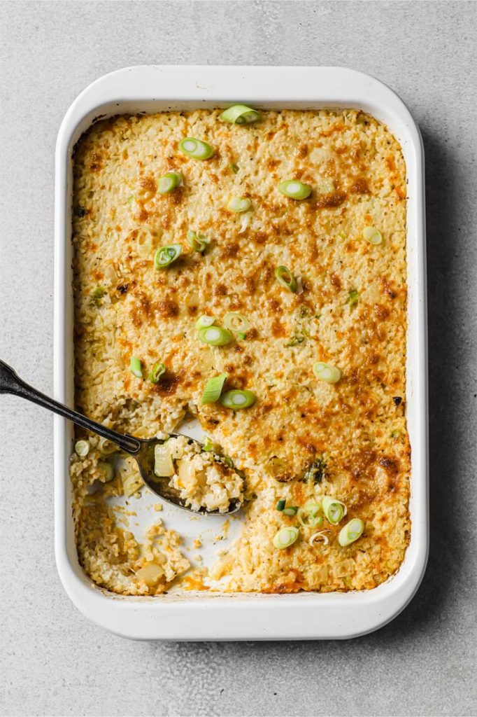overhead shot of sour cream and onion cauliflower bake in baking pan with spoon atop a marble board