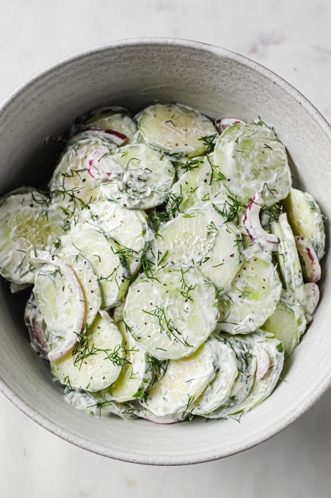 Overhead shot of Creamy Dill Cucumber Salad in a ceramic bowl a marble countertop