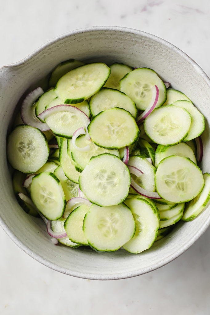 Overhead shot of mixed sliced cucumbers and red onions in a ceramic bowl
