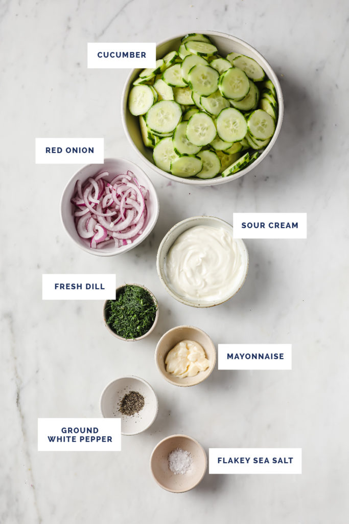 Overhead shot of labeled ingredients for dill salad on a marble countertop