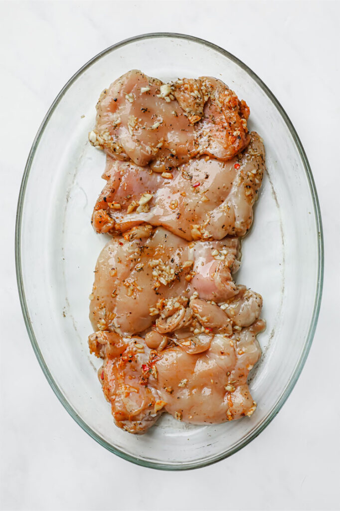 Overhead shot of marinated chicken thighs in a glass baking pan. The baking pan is resting on a marble countertop.