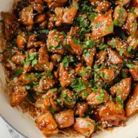 Close-up shot of a large pan with the sweet sticky chicken thighs garnished with freshly-cracked pepper, sesame seeds, and fresh parsley.