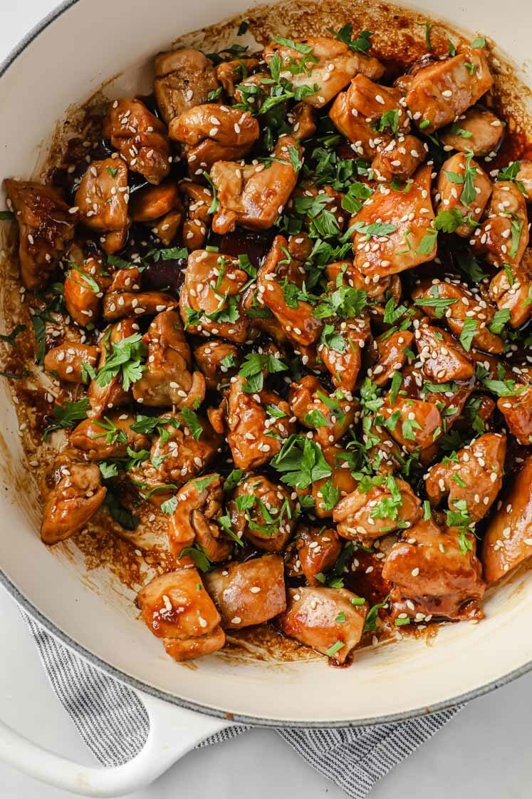 Close-up shot of a large pan with the sweet sticky chicken thighs garnished with freshly-cracked pepper, sesame seeds, and fresh parsley.