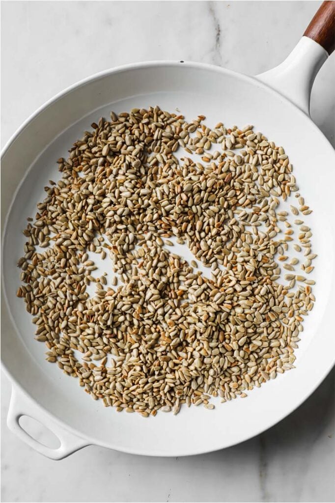 Overhead shot of toasted sunflower seeds in a large pan, atop a marble counter.