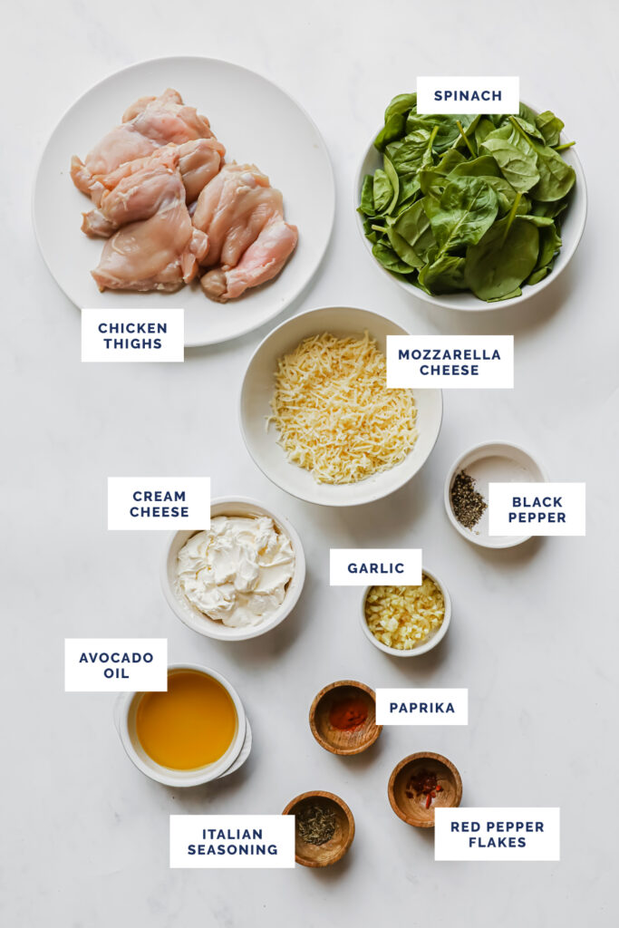 Overhead shot of labeled ingredients for the Low-Carb Creamy Spinach Chicken Bake on a marble countertop.