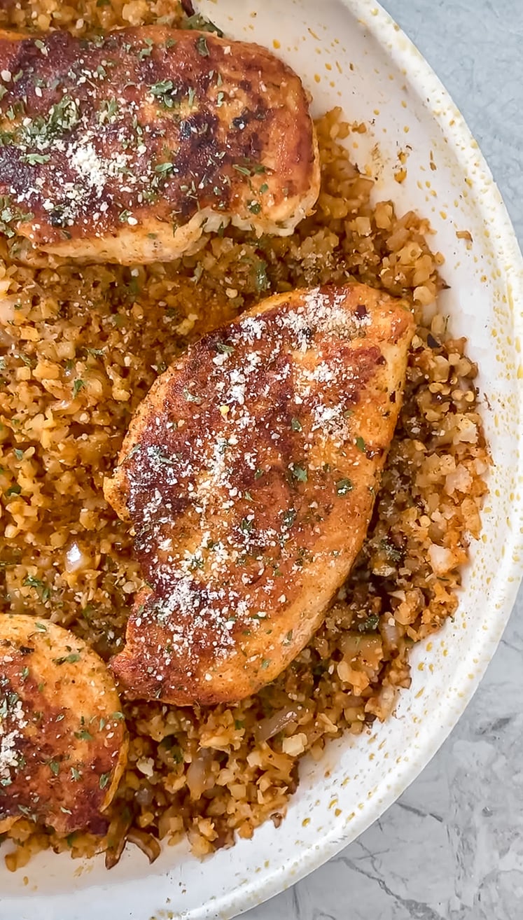 overhead shot of cooked chicken breast in pan atop cauliflower rice