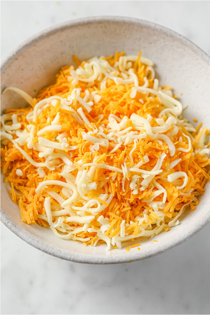 Overhead shot of a small bowl with mixed shredded cheeses, atop a marble countertop.