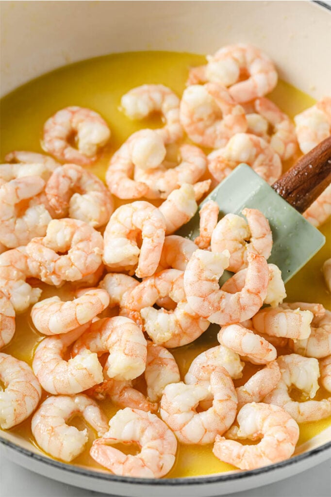 Overhead shot of a cooking pot with deveined shrimps as they are flipped by a cooking spatula.