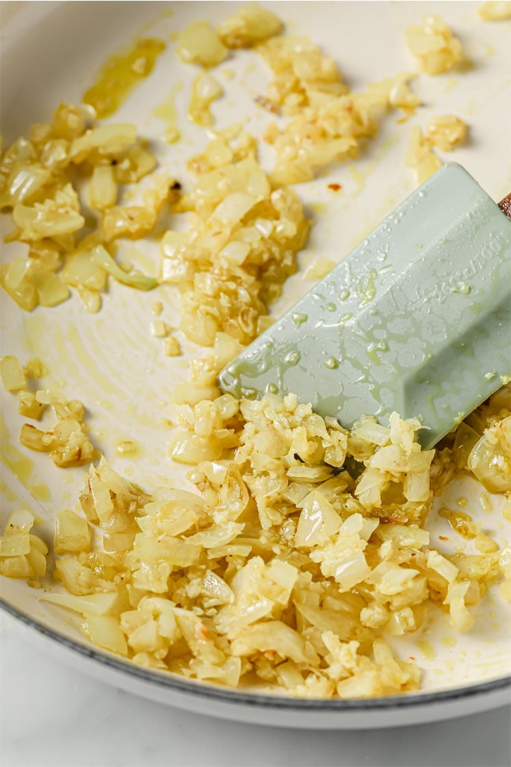 Overhead shot of a cooking pot with chopped onions and minced garlic as they are sauteed by a cooking spatula.