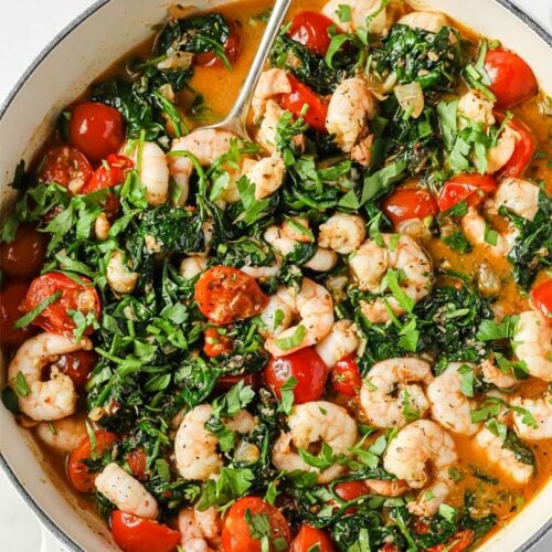Overhead shot of the One-Pan Low-Carb Tuscan Garlic Shrimp, garnished with chopped fresh parsley and Italian seasoning, served in a cooking pot with a serving spoon.