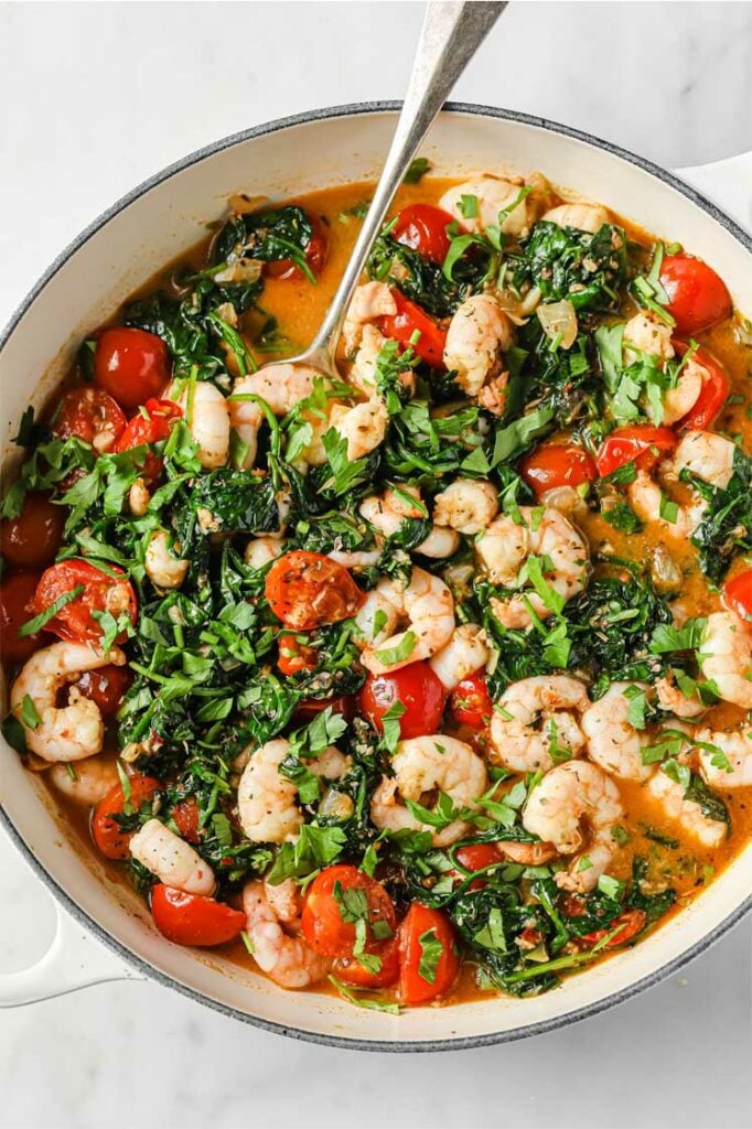 Overhead shot of the One-Pan Low-Carb Tuscan Garlic Shrimp, garnished with chopped fresh parsley and Italian seasoning, served in a cooking pot with a serving spoon.