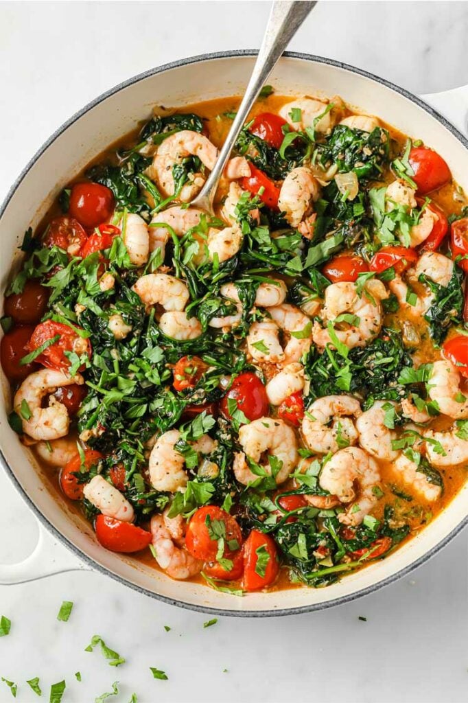 Overhead shot of the One-Pan Low-Carb Tuscan Garlic Shrimp, garnished with chopped fresh parsley and Italian seasoning, served in a cooking pot with a serving spoon.