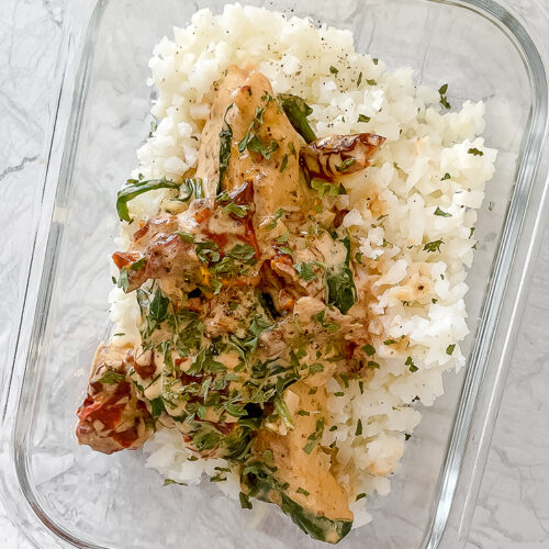 overhead shot of meal prep container with tuscan chicken and cauliflower rice atop marble countertop