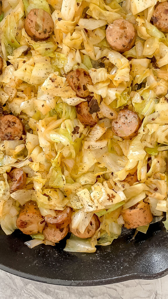 overhead shot of chicken sausage and cabbage skillet in cast-iron skillet atop marble countertop