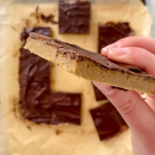 side angle shot of hand holding 1 no-bake sunflower seed butter bar over top of other sliced bars atop cutting board on marble counterop