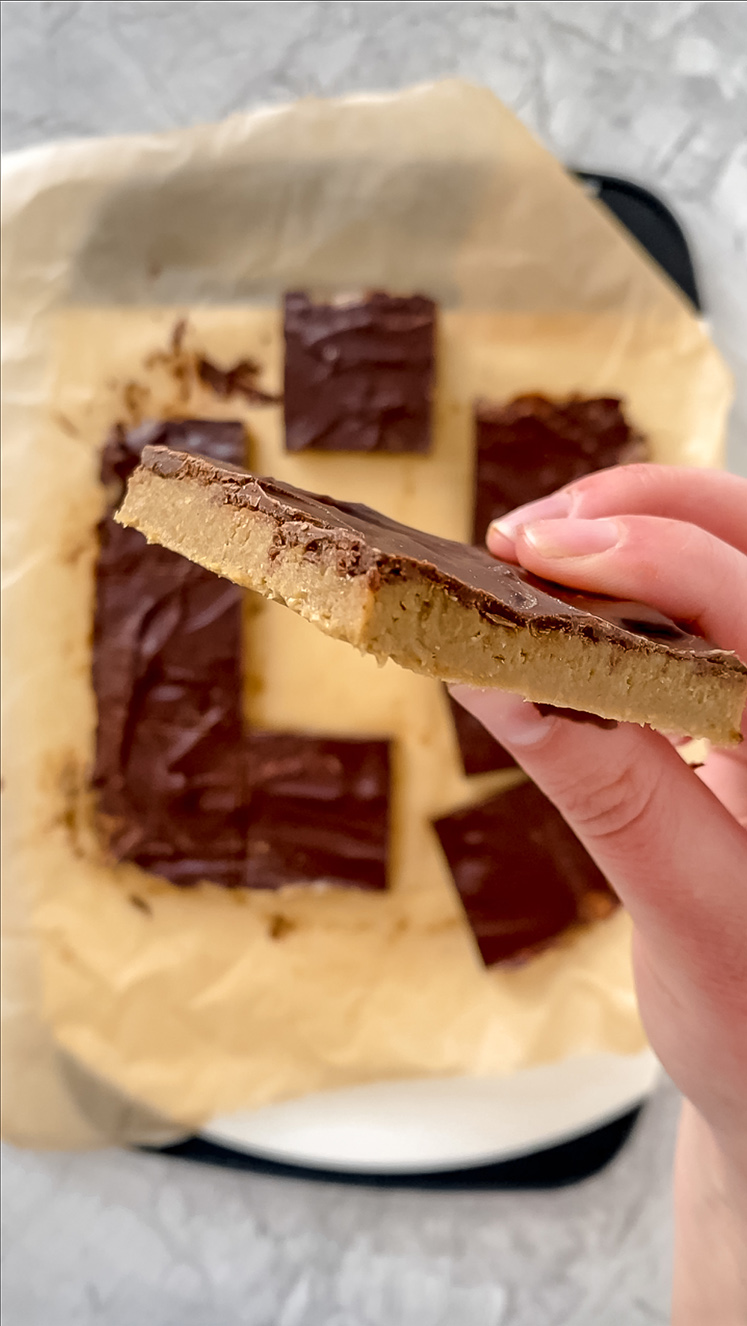 side angle shot of hand holding 1 no-bake sunflower seed butter bar over top of other sliced bars atop cutting board on marble counterop