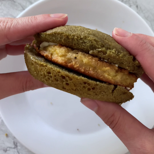 Overhead shot of 90-second low-carb bread sandwich held over a plate, atop marble countertop.