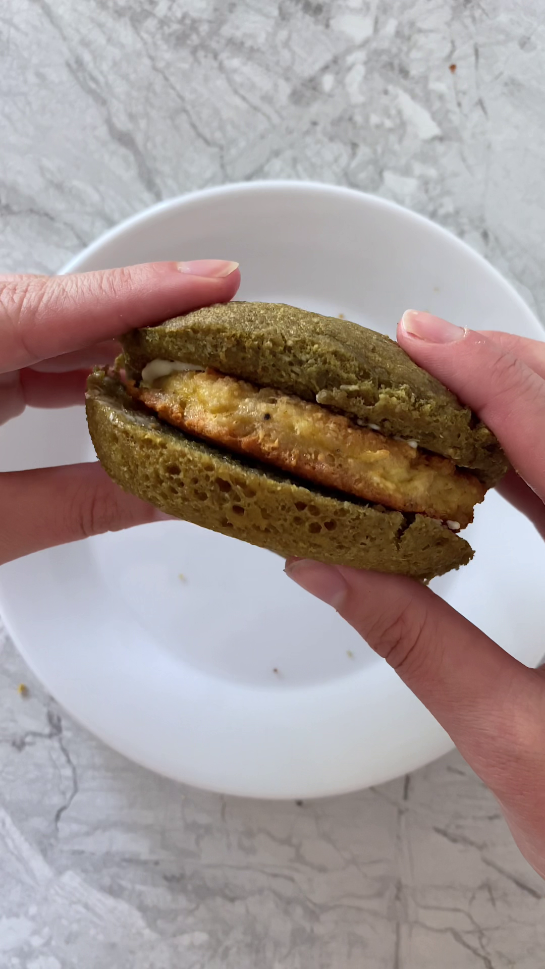 Overhead shot of 90-second low-carb bread sandwich held over a plate, atop marble countertop.