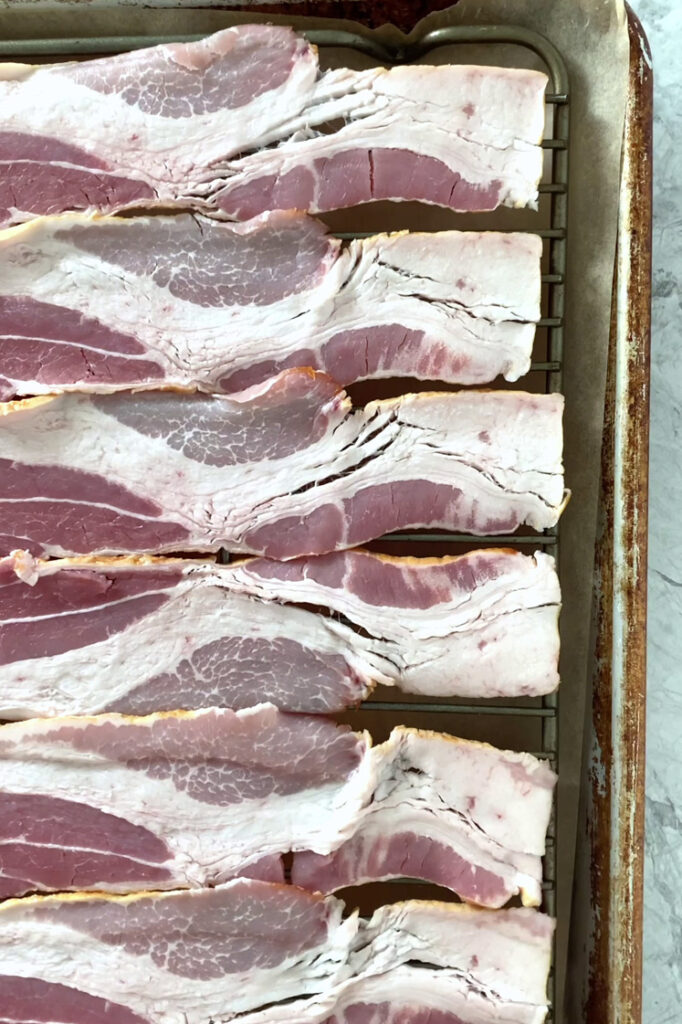Overhead shot of bacon slices arranged in an even layer atop a wire rack. The wire rack rests inside a parchment paper-lined baking sheet.