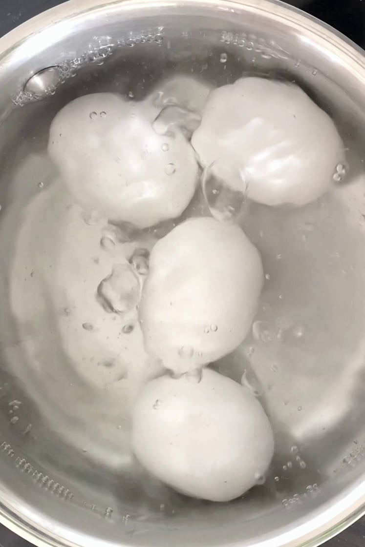 Overhead shot of a saucepan with boiling water and four eggs.