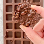 overhead shot of hand holding prepared 2-ingredient chocolate and sunflower seed bites above silicone mold atop marble countertop