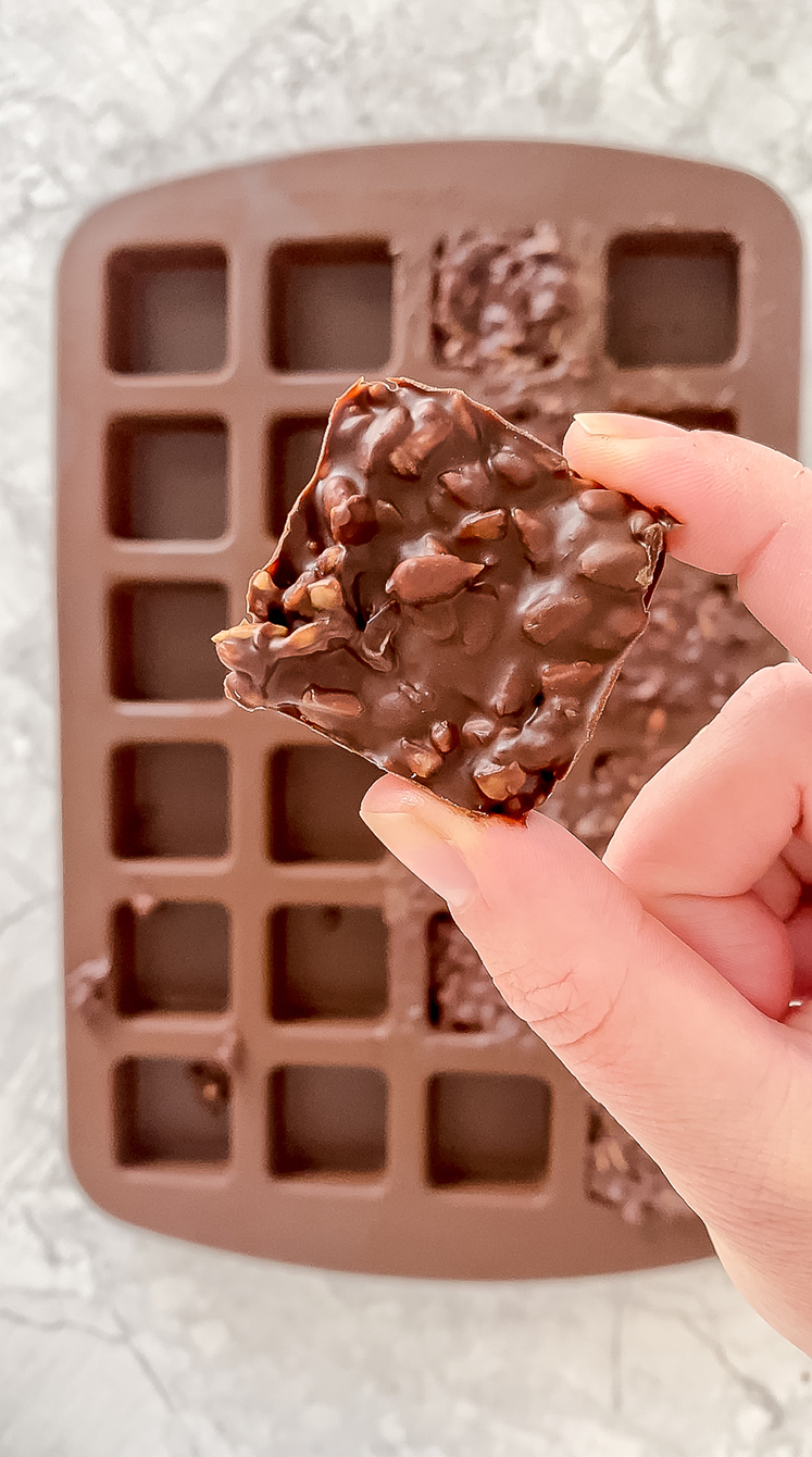 overhead shot of hand holding prepared 2-ingredient chocolate and sunflower seed bites above silicone mold atop marble countertop