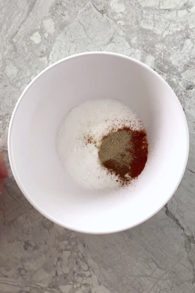 Overhead shot of a small bowl with allulose, cayenne pepper, cinnamon, and pepper. The small bowl sits atop a marble countertop.