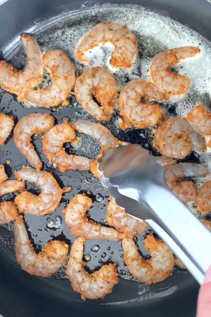 Overhead shot of a pan with shrimps as they are being cooked and flipped by tongs.