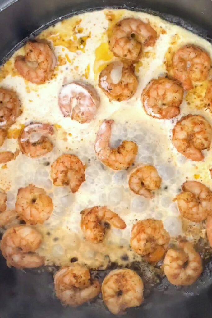 Overhead shot of a pan with shrimps and heavy cream as they are being cooked.