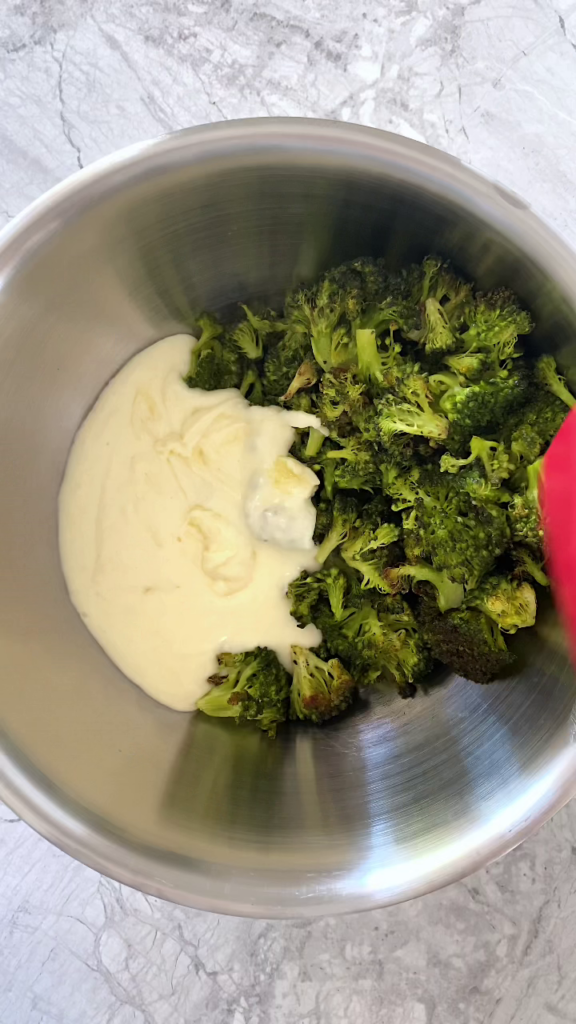 Overhead shot of a stainless steel bowl with cheese sauce and broccoli, atop a marble countertop.