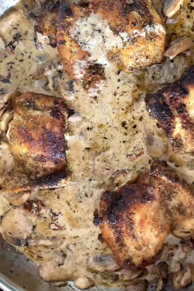Overhead shot of a pan with seasoned creamy mushroom sauce and cooked chicken thighs.