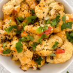 overhead shot of prepared bang bang cauliflower in white bowl garnished with fresh parsley and black sesame seeds atop marble countertop