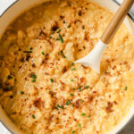 overhead shot of prepared cauliflower soup in pot garnished with chives with spoon in pot atop marble countertop