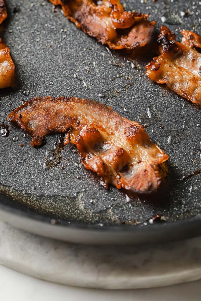 Overhead shot of a large pan with bacon slices cooked until crispy. The pan sits atop a marble countertop.