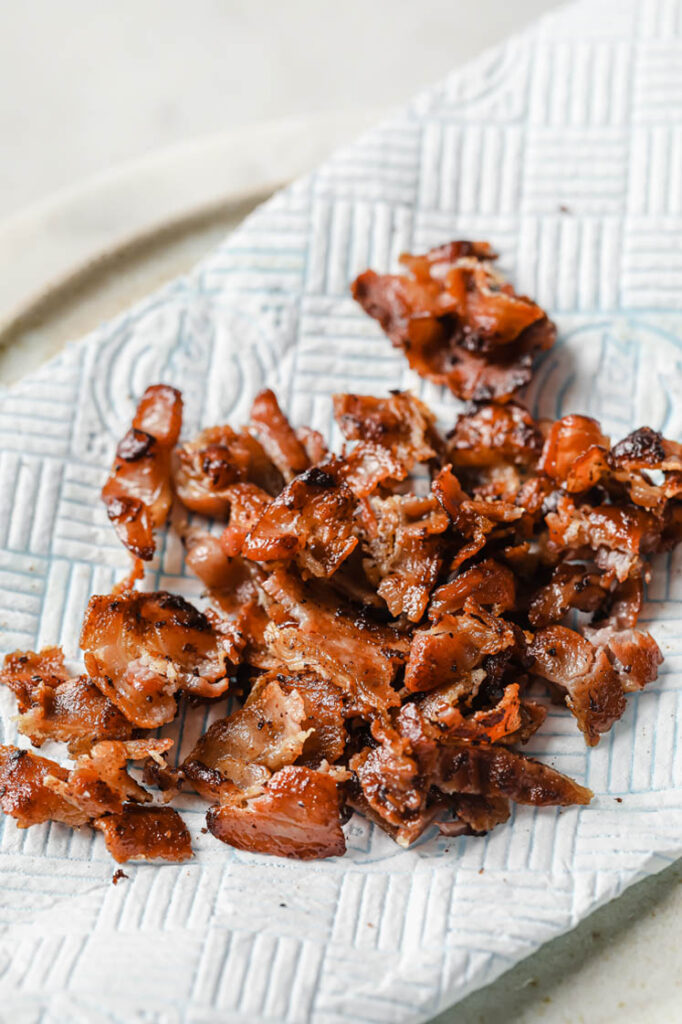 Overhead shot of a towel-lined ceramic plate with crumbled bacon. The plate rests atop a marble countertop.