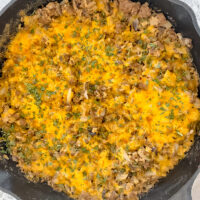 overhead shot of cooked creamy ground beef and cauliflower rice in cast iron skillet next to a linen atop a marble countertop