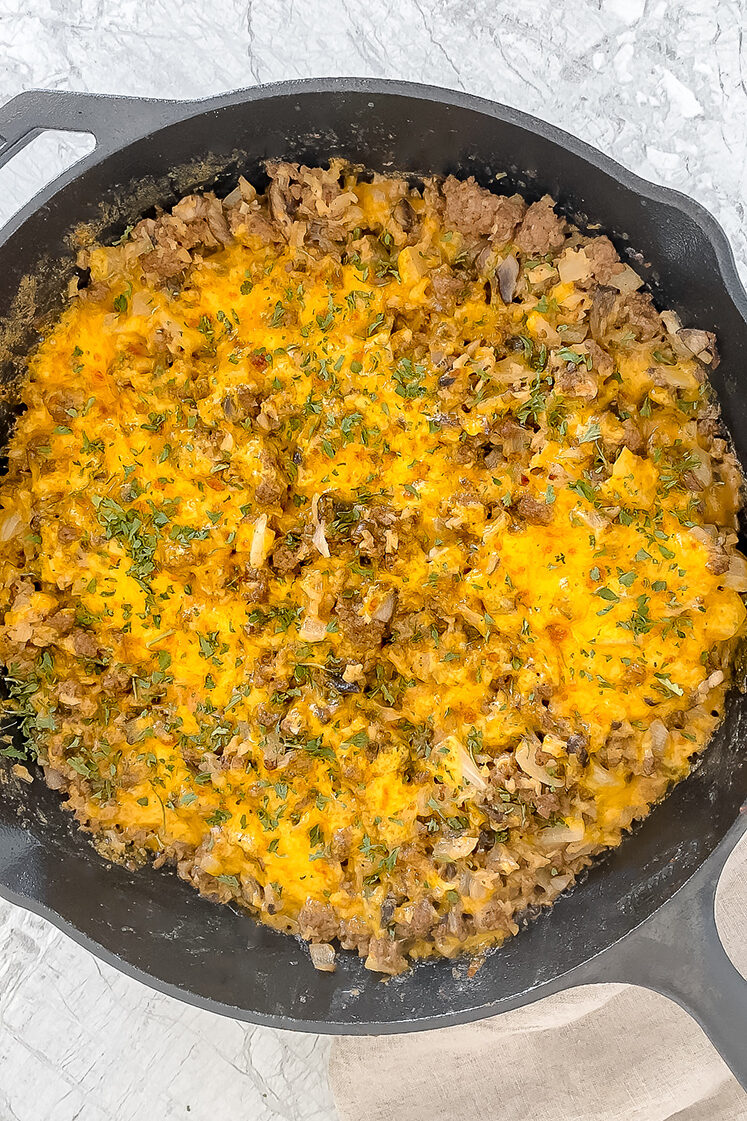 overhead shot of cooked creamy ground beef and cauliflower rice in cast iron skillet next to a linen atop a marble countertop