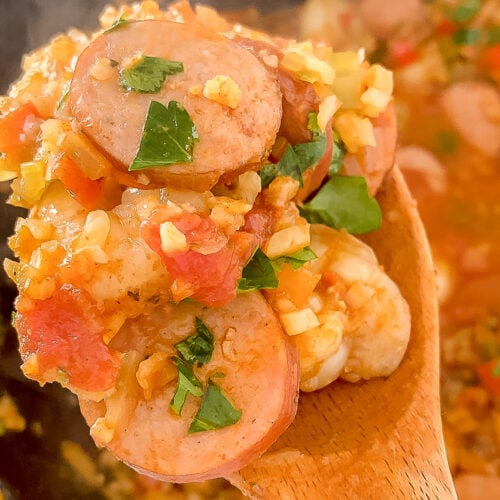 overhead shot of wooden spoon with cooked jambalaya garnished with parsley atop jambalaya in cast iron skillet