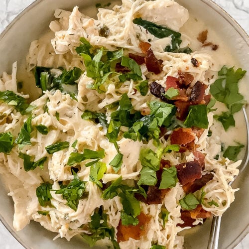 overhead shot of bowl of garnished chicken bacon spinach soup with spoon atop marble countertop