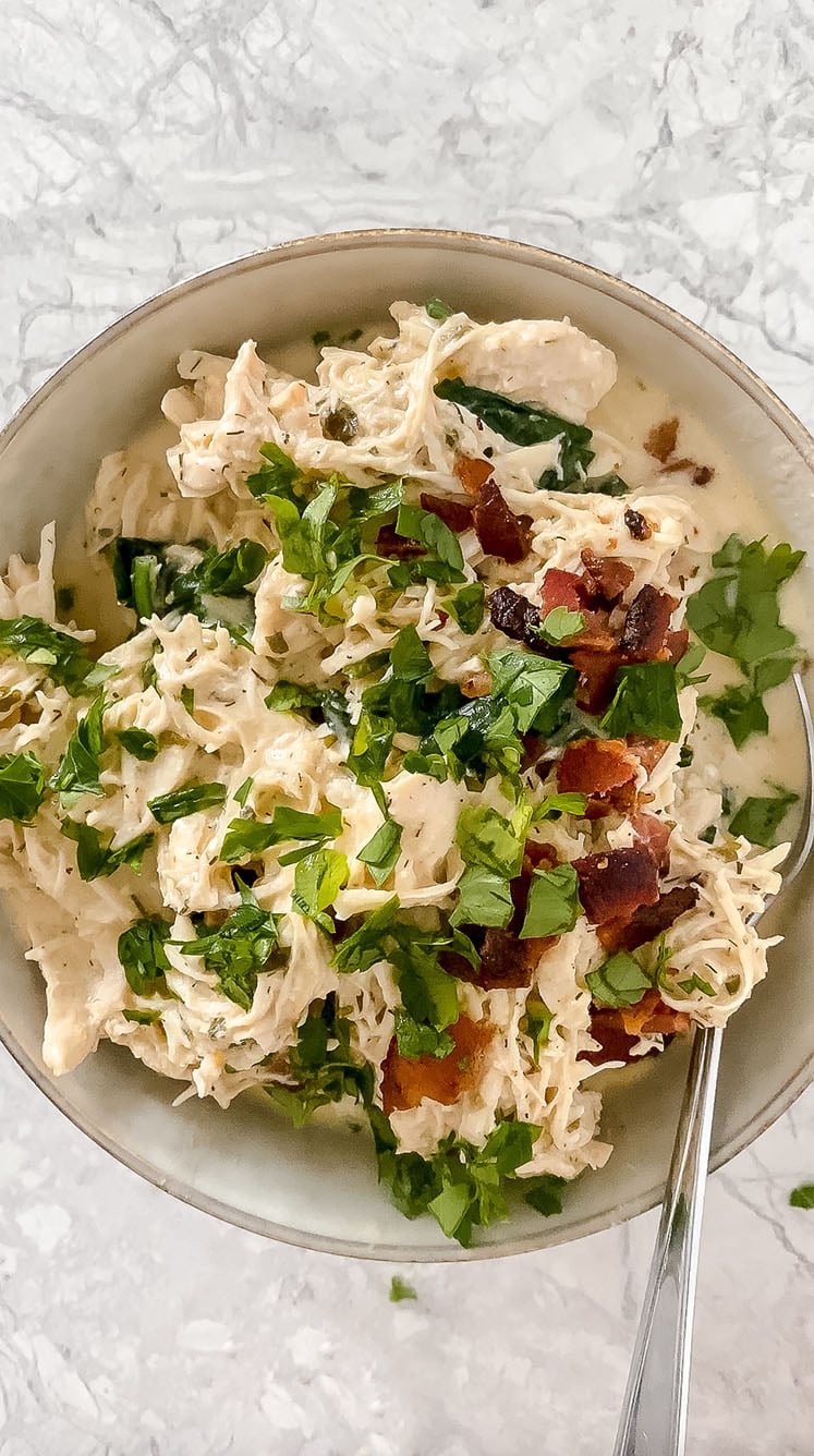 overhead shot of bowl of garnished chicken bacon spinach soup with spoon atop marble countertop