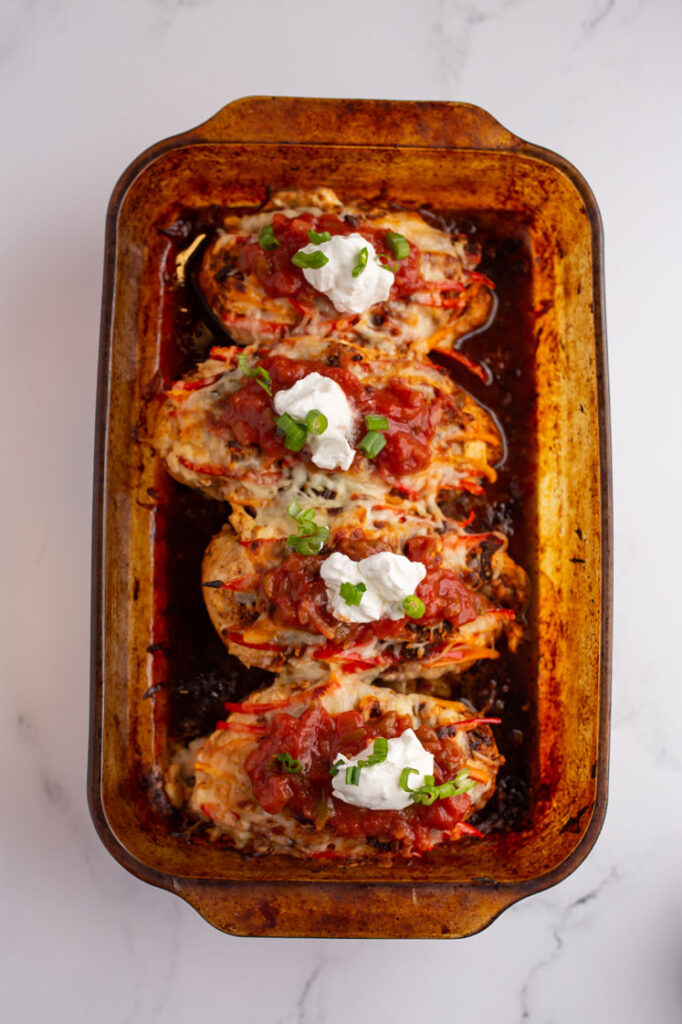 Overhead shot of a baking pan with cheesy chicken fajita bake, garnished with sour cream, salsa and finely chopped green onions. The baking pan rests atop a marble countertop.