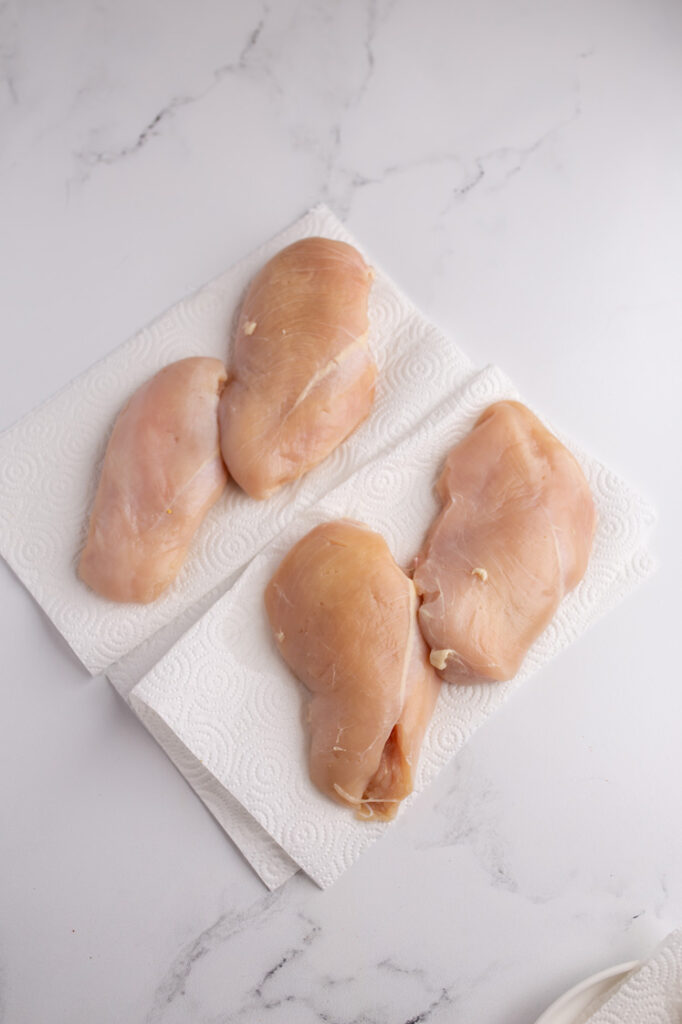 Overhead shot of chicken breasts on a paper towels atop a marble countertop.
