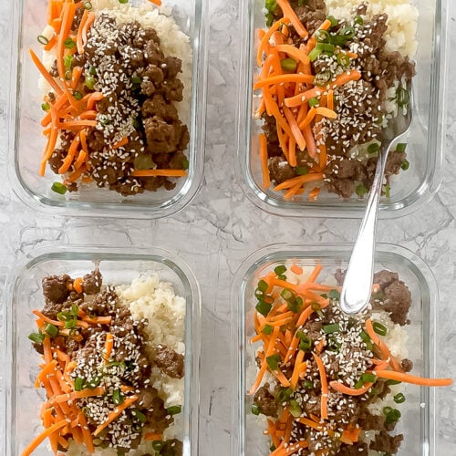 Overhead shot of meal prep containers with garnished Korean ground beef bowls atop marble countertop.