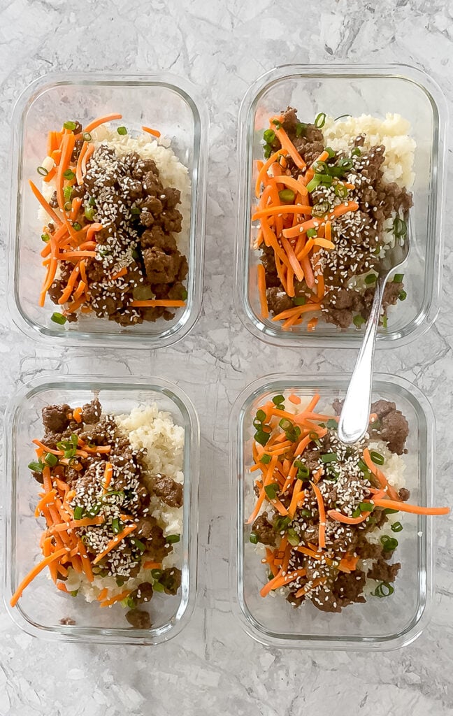 overhead shot of meal prep containers with garnished korean ground beef bowls atop marble countertop