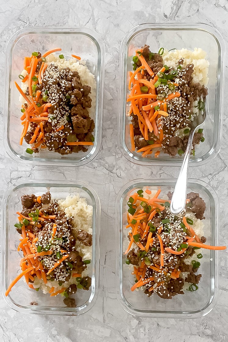 overhead shot of meal prep containers with garnished korean ground beef bowls atop marble countertop