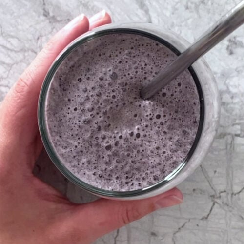 Overhead shot of the low-carb blueberry spinach smoothie in a glass with a straw atop a marble countertop.